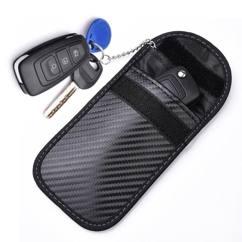 Etui antykradzieżowe RFID na pilota samochodowego leżące obok kluczyka keyless na masce auta przed wjazdem na parking